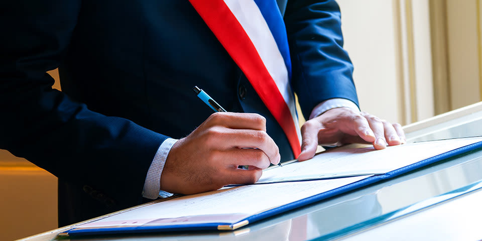 Signature d'un document officiel par un maire portant son écharpe tricolore